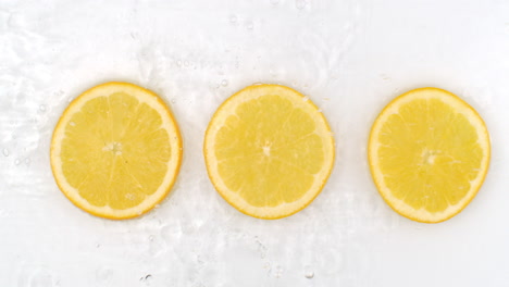 Slow-motion-water-splash-on-three-slices-of-orange-lying-on-a-white-background-in-water